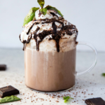 Homemade café mocha latte in a clear mug topped with foam and a sprinkle of cocoa powder.