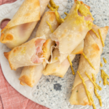 Golden brown ham-wrapped mozzarella cheese sticks cooked in an air fryer, served on a plate with dipping sauce.