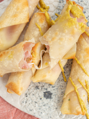 Golden brown ham-wrapped mozzarella cheese sticks cooked in an air fryer, served on a plate with dipping sauce.