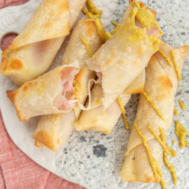 Golden brown ham-wrapped mozzarella cheese sticks cooked in an air fryer, served on a plate with dipping sauce.
