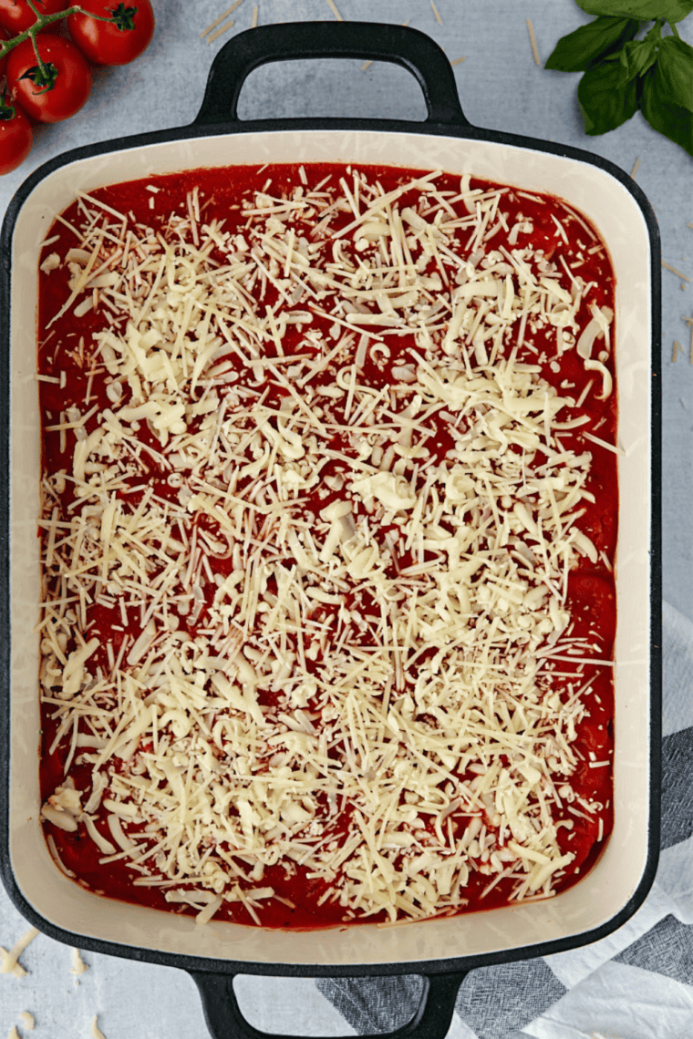 Spreading spaghetti sauce in a baking dish and arranging stuffed manicotti before topping with more sauce.