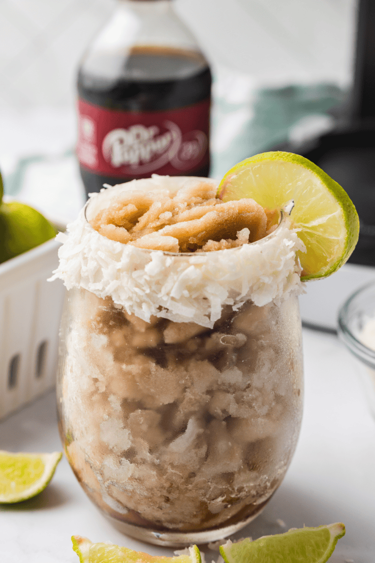 Frosty Ninja Creami Dirty Dr Pepper Slush in a glass, topped with a lime wedge and served with a straw