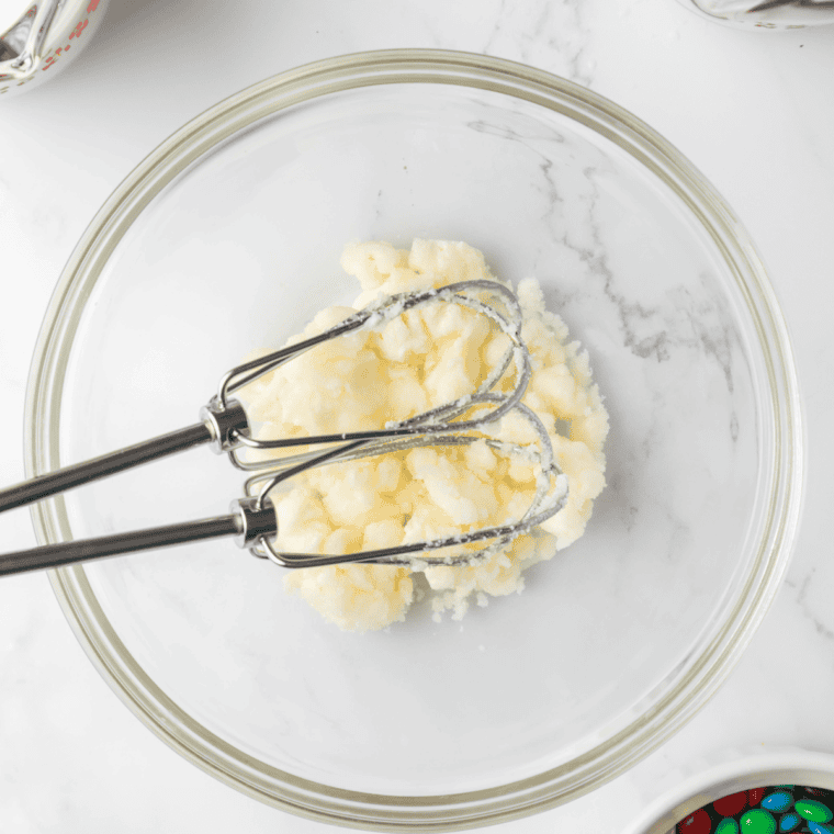 Adding granulated sugar and vanilla extract to softened cream cheese and mixing until fully combined in a bowl