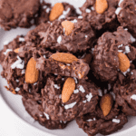 Close-up of Slow Cooker Almond Joy Chocolate Clusters made with melted chocolate, shredded coconut, and whole almonds, arranged on parchment paper.