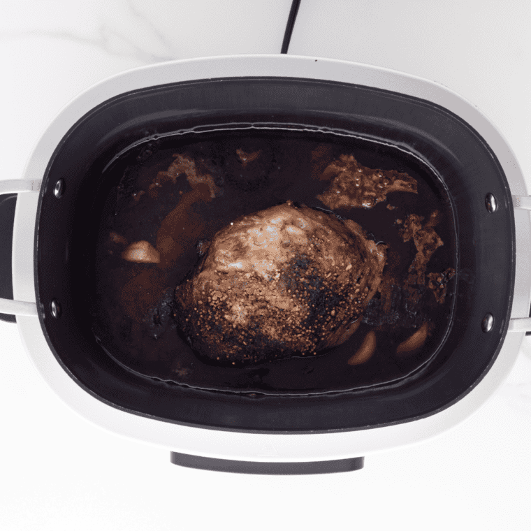 Seasoned corned beef in a slow cooker topped with spices, brown sugar, and whole garlic cloves