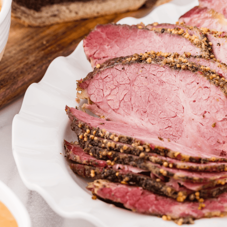 Sliced slow cooker pastrami with a peppery crust on a wooden board, ready for sandwiches