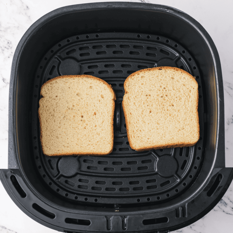 Placing slices of bread in the air fryer basket, ensuring they don't overlap.