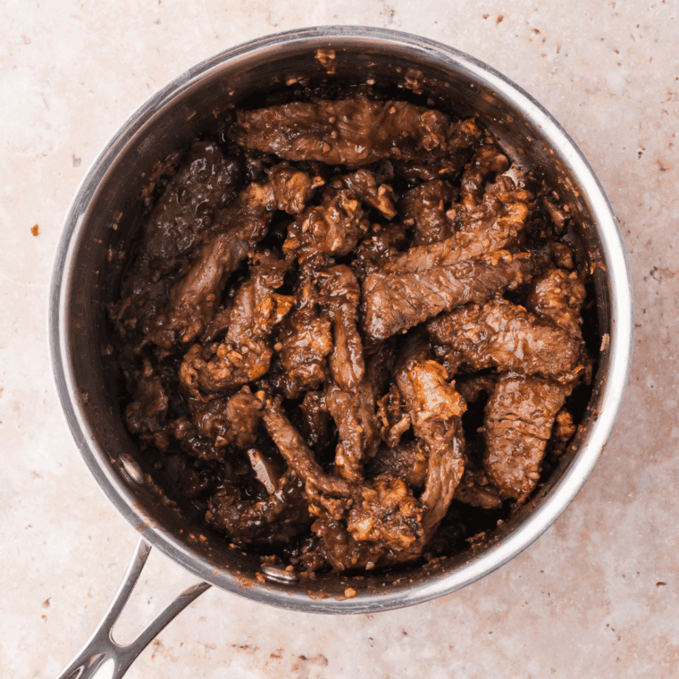 Tossing crispy beef in sauce and garnishing with green onions and sesame seeds.