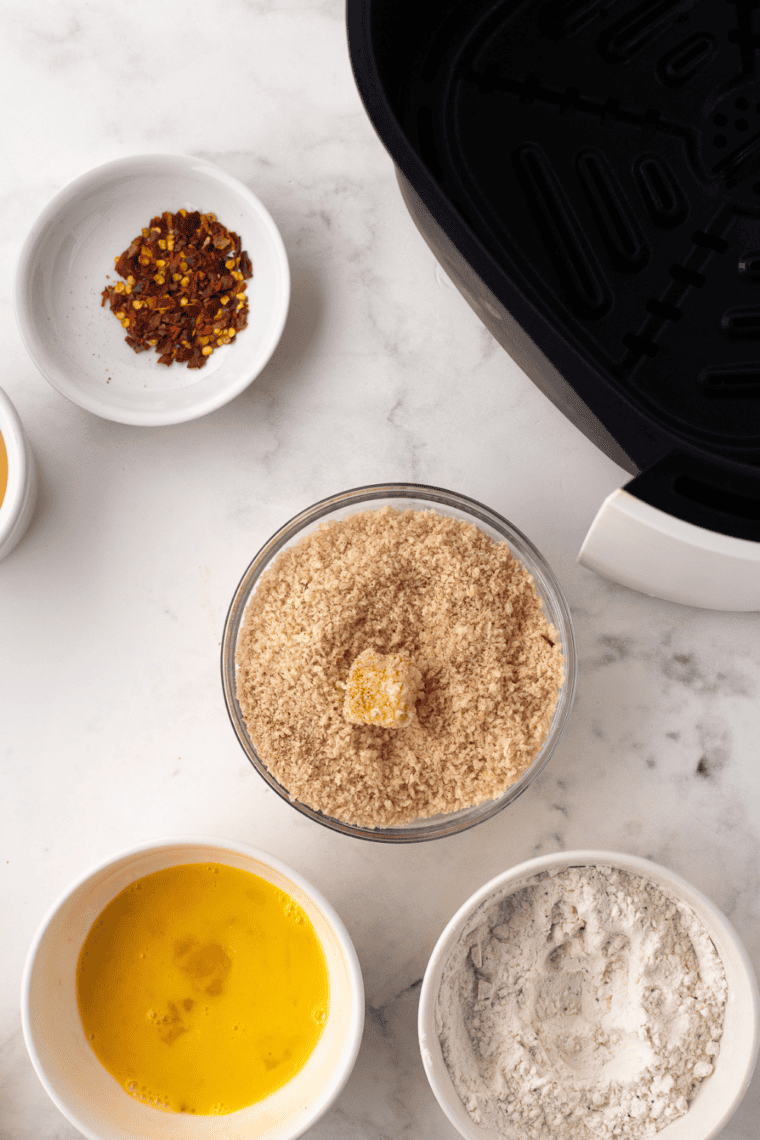 Coating halloumi cubes in flour, egg, and breadcrumb mixture for crispy texture.