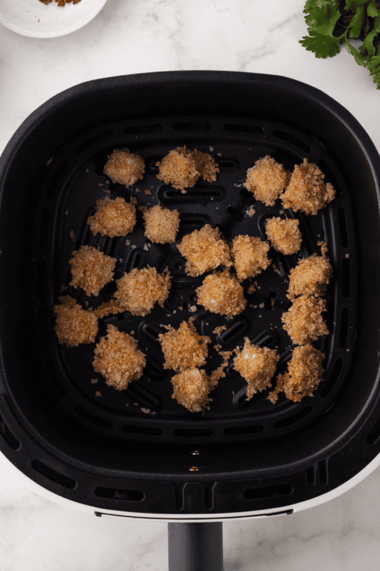 Placing breaded halloumi bites in the air fryer basket and spraying with olive oil.