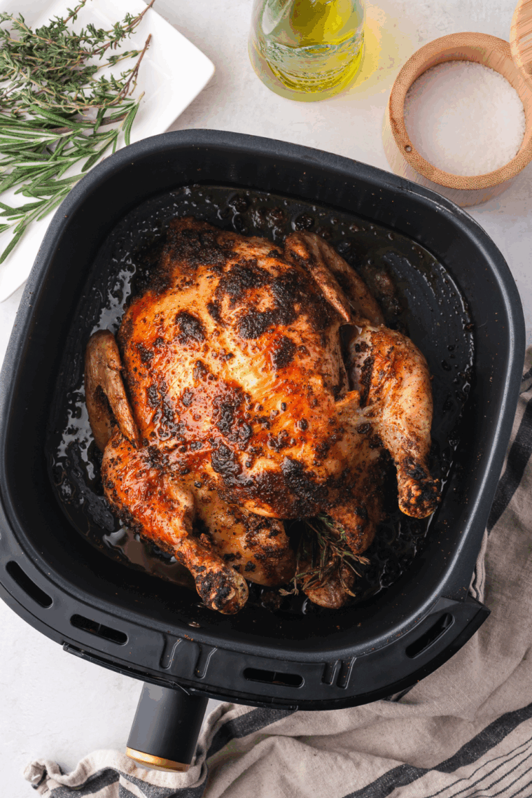 Golden, crispy whole chicken cooked from frozen in the air fryer, resting in the air fryer basket.