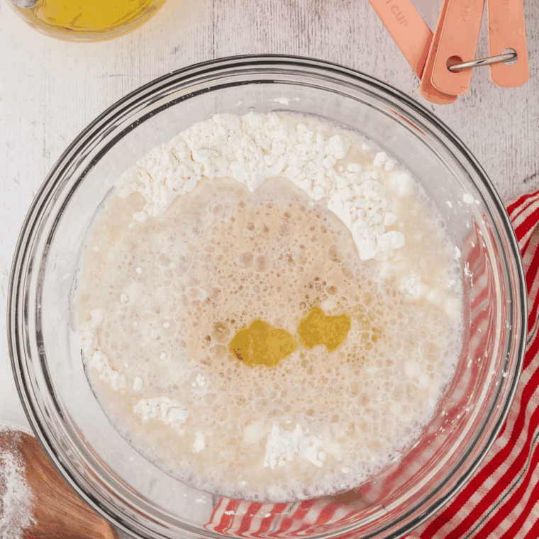 Creating a well in dry ingredients and mixing with yeast mixture and olive oil to form sticky dough for gluten-free bread.