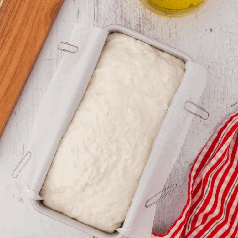 Transferring sticky dough into a loaf pan and smoothing the top with a wet spatula for gluten-free bread.