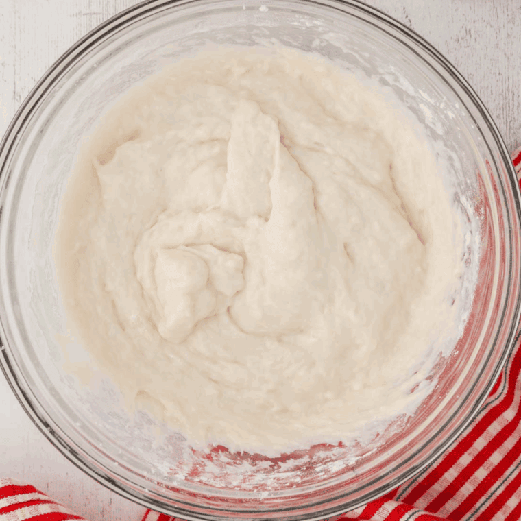 Mixing the yeast mixture and olive oil into dry ingredients to form sticky dough for gluten-free bread.