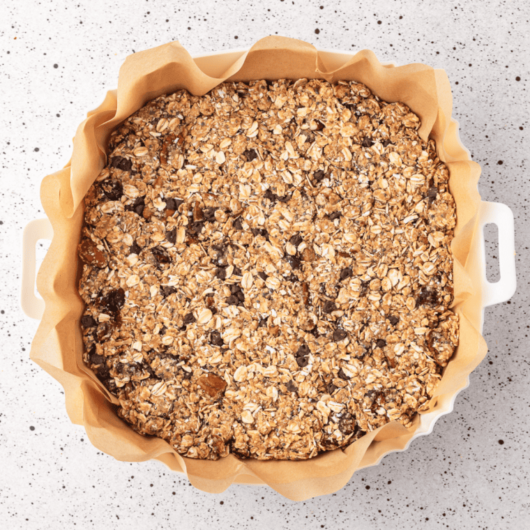 Lining a small baking dish with parchment paper and pressing granola mixture into an even layer.