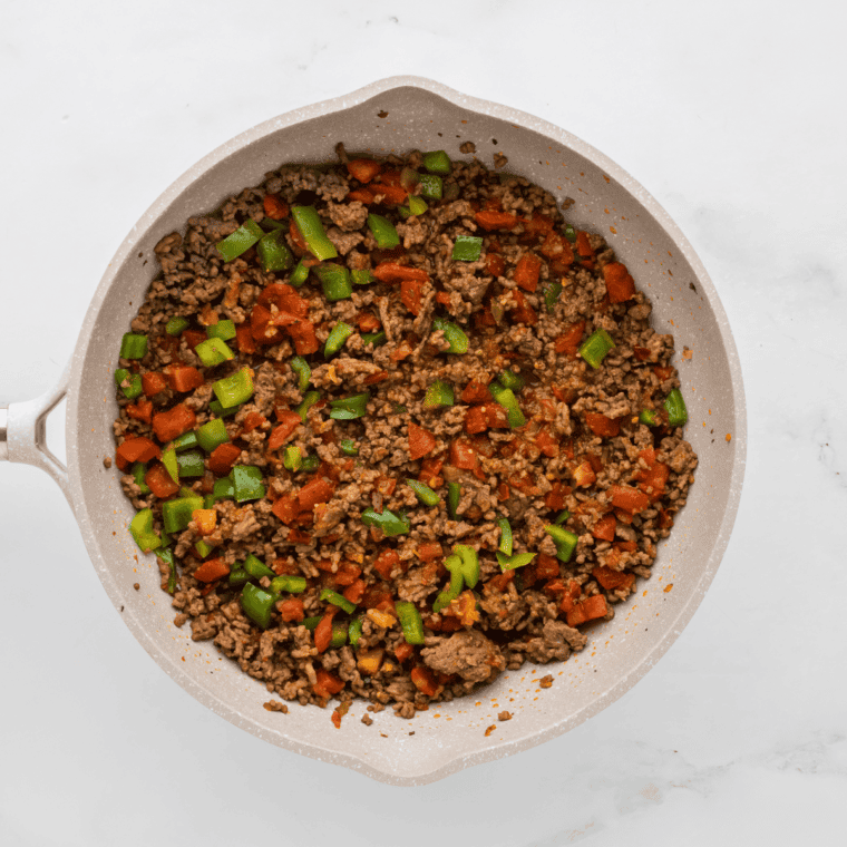 Browning ground beef with bell peppers, diced tomatoes, and taco seasoning in a skillet.
