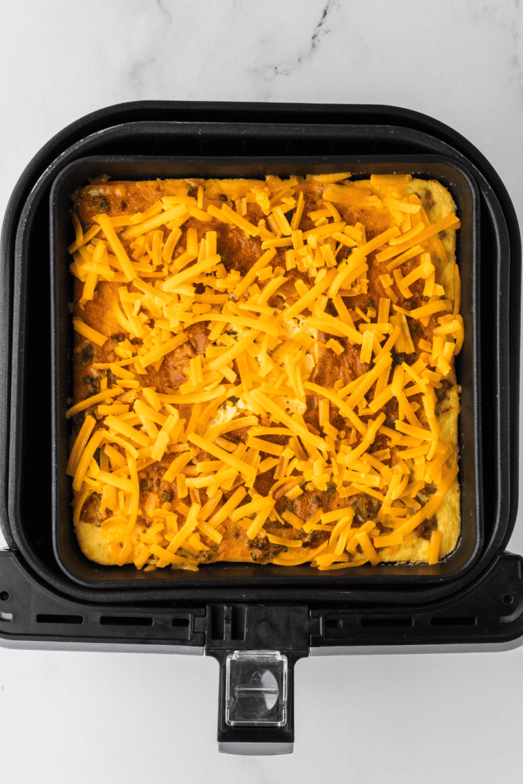 Sprinkling shredded cheddar cheese on top of the casserole to melt.