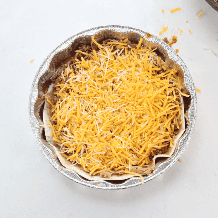 Layering tortillas, beef mixture, cheese, and enchilada sauce in a greased air fryer-safe dish.