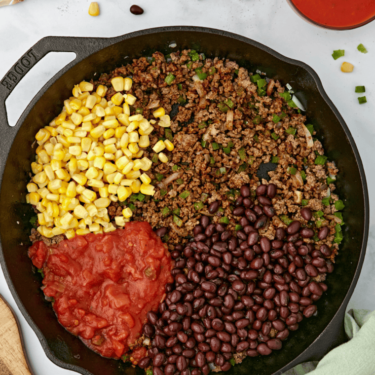 Adding black beans, corn, beef broth, salsa, and tomato sauce to the skillet, then stirring in rice.
