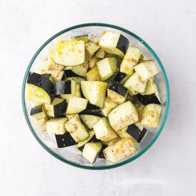Tossing eggplant cubes with olive oil, salt, and pepper before placing them in a single layer in the air fryer basket.