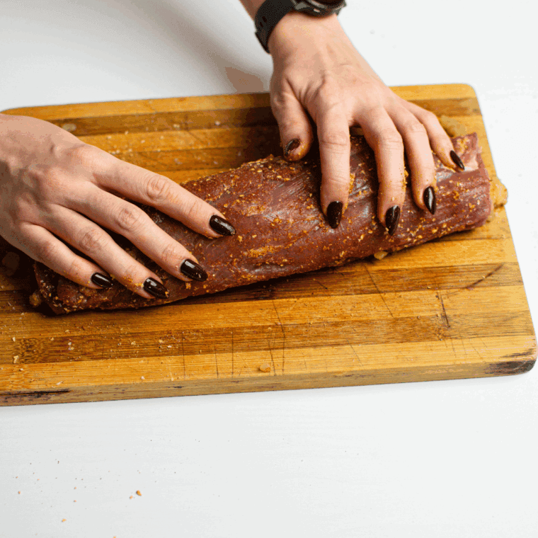 Making a slit along the pork tenderloin to create a pocket, then filling it with apple stuffing and securing the opening with toothpicks.
