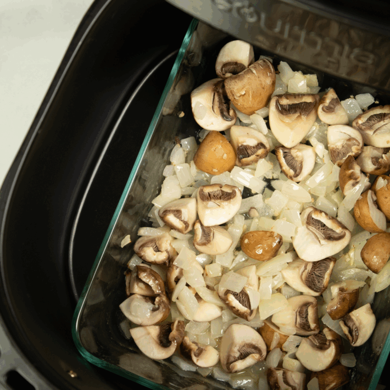Quartered mushrooms being added to the onion-garlic mixture in the baking pan.