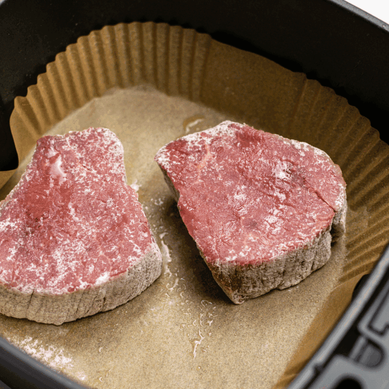 Coating steaks with olive oil, placing in air fryer basket, and cooking at 400°F.
