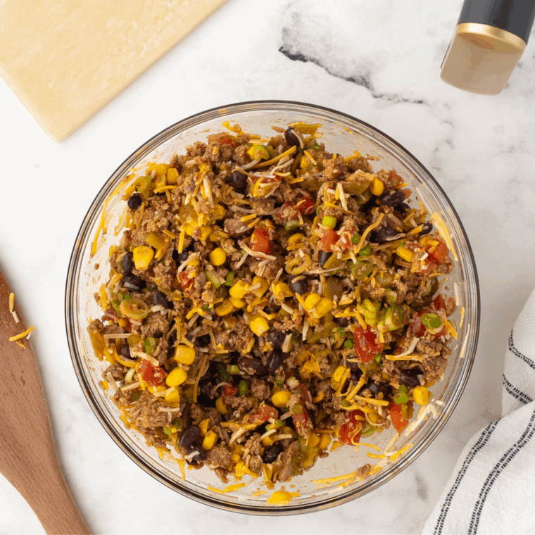Combining cooked ground meat, cheese, black beans, corn, tomatoes, green chilies, and green onions in a bowl, then seasoning with salt and pepper.