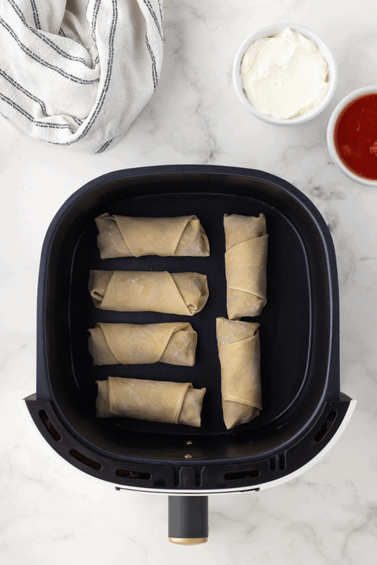 Preheating air fryer to 390°F, spraying the basket with cooking spray, and placing egg rolls in a single layer to air fry.