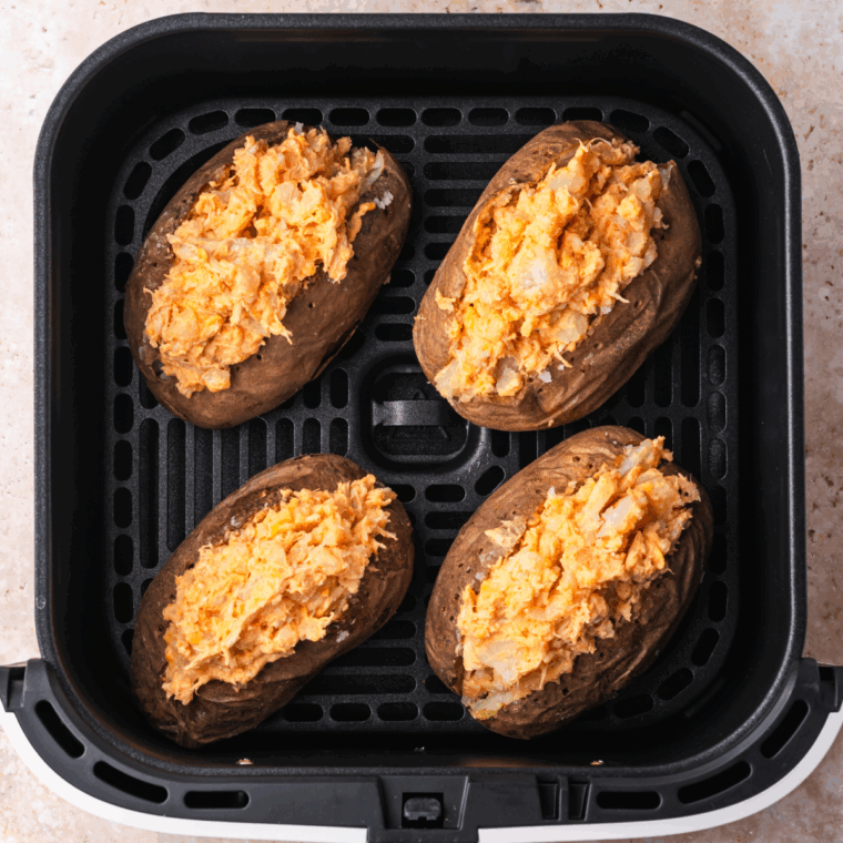 Cutting cooked potatoes in half and scooping out the insides to mix with buffalo chicken filling.