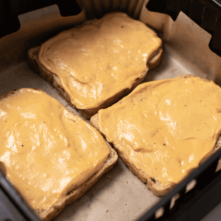 Placing slices of bread in the air fryer basket and spooning cheese sauce generously over each slice.