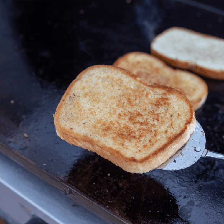 Golden brown slices of toast cooking on a Blackstone griddle.