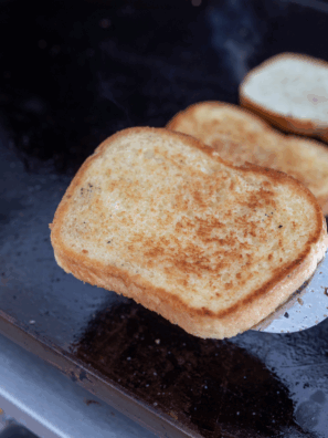 Crispy slices of golden toast cooking on a Blackstone griddle.