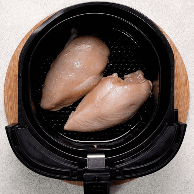 Chicken breasts brushed with olive oil and placed in the air fryer basket, cooking.