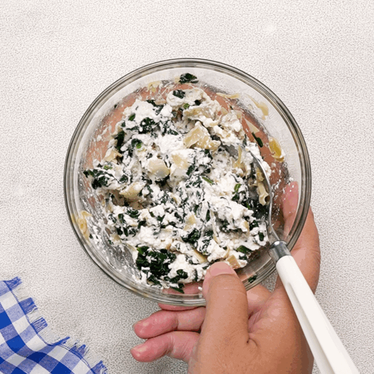 Goat cheese, chopped spinach, and artichoke hearts mixed in a bowl for topping.