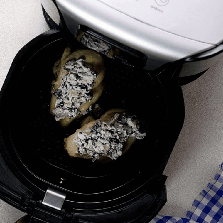 Goat cheese mixture being added on top of cooked chicken breasts, ready for the air fryer.