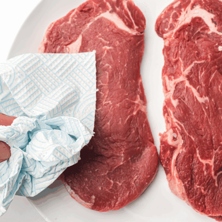 Patting steaks dry with paper towels and seasoning with salt and pepper, allowing them to rest at room temperature before cooking.