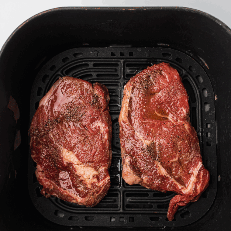 Preheating air fryer to 400°F, brushing steaks with olive oil, and air frying for 8-10 minutes for medium-rare doneness, flipping halfway through.