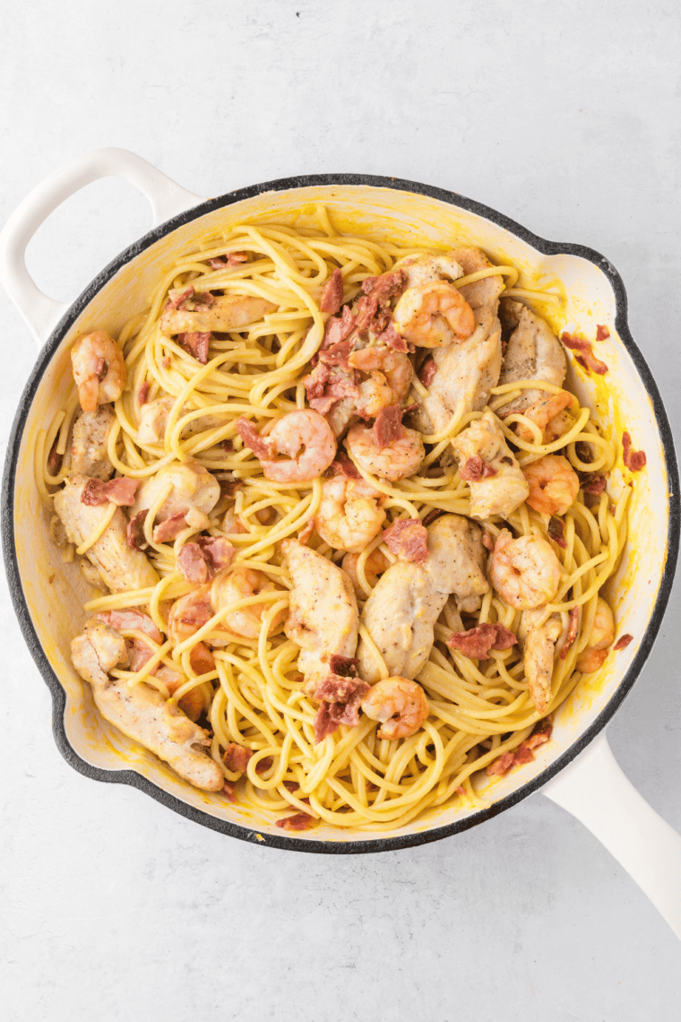 Combine cooked spaghetti and crumbled bacon in a skillet. Slowly pour in egg yolk mixture, stirring to coat pasta evenly, and toss in cooked chicken and shrimp.