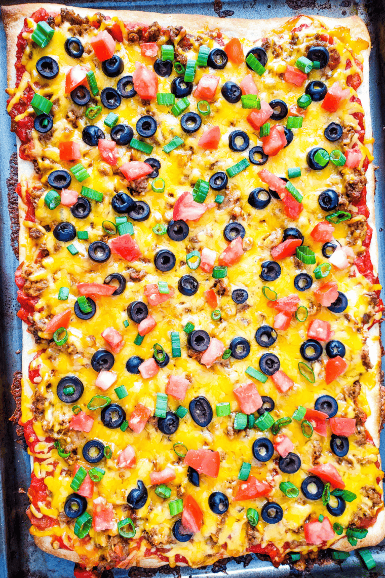 Easy taco pizza topped with seasoned ground beef, melted cheddar, olives, diced tomato, and green onions, cut into slices
