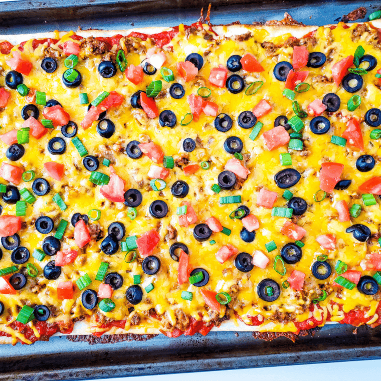Sliced taco pizza with seasoned beef, melted cheddar cheese, and fresh toppings, served with sour cream