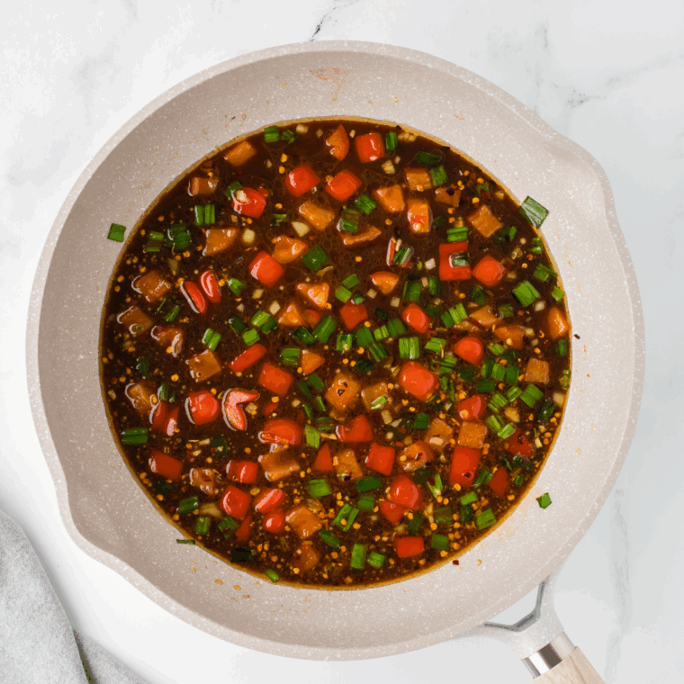 Sautéing garlic, green onions, and red bell pepper in vegetable oil, adding sauce and air-fried chicken, then tossing in cooked spaghetti to coat with sauce.