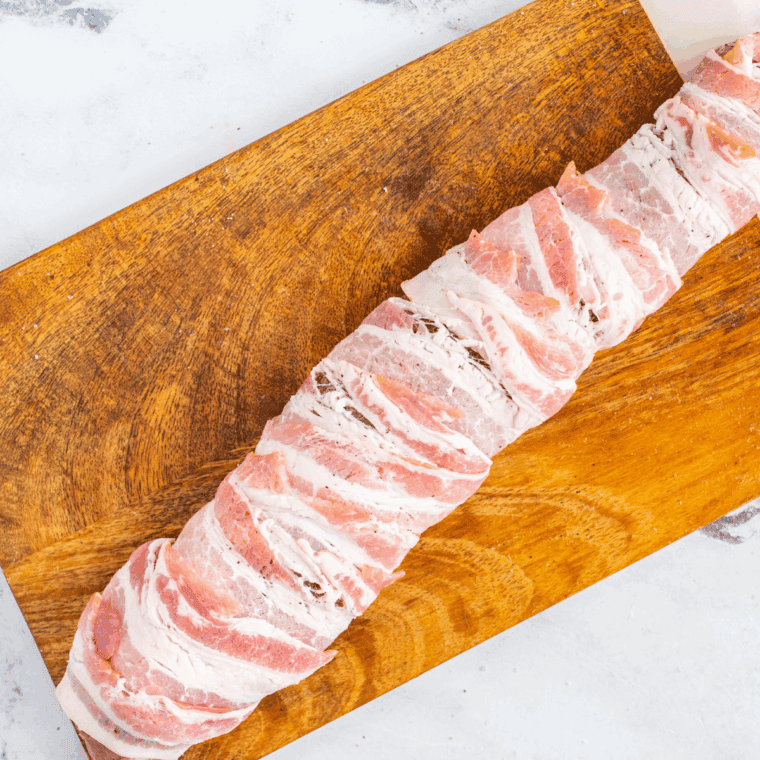 Wrapping pork tenderloin with bacon strips and securing with toothpicks.