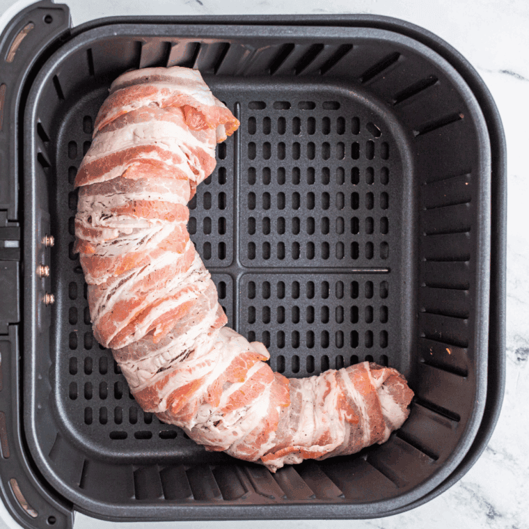 Placing wrapped pork tenderloin in the air fryer and cooking at 380°F.