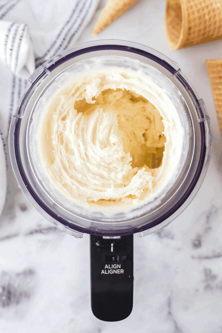 Placing frozen mixture into Ninja Creami and processing until smooth and creamy.