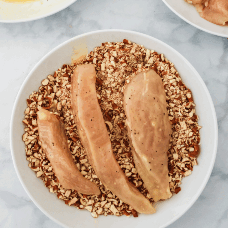 Shake 'N Bake Crunchy Pretzel Seasoned Coating Mix ingredients in a bowl, with chicken tenders on top.