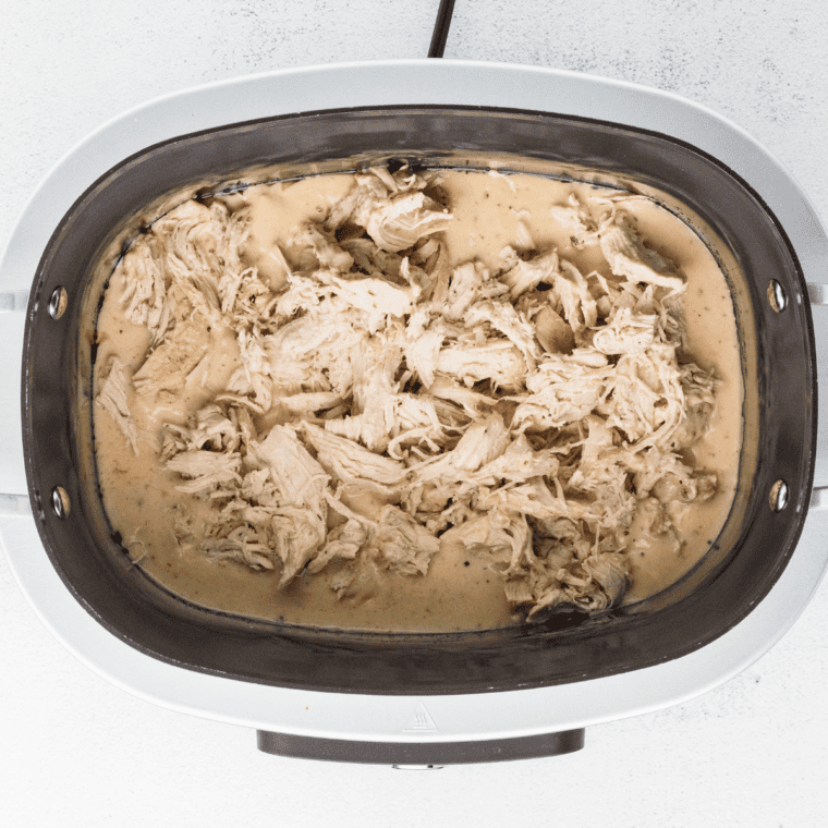 Shredding cooked chicken with two forks in the slow cooker and stirring to combine.