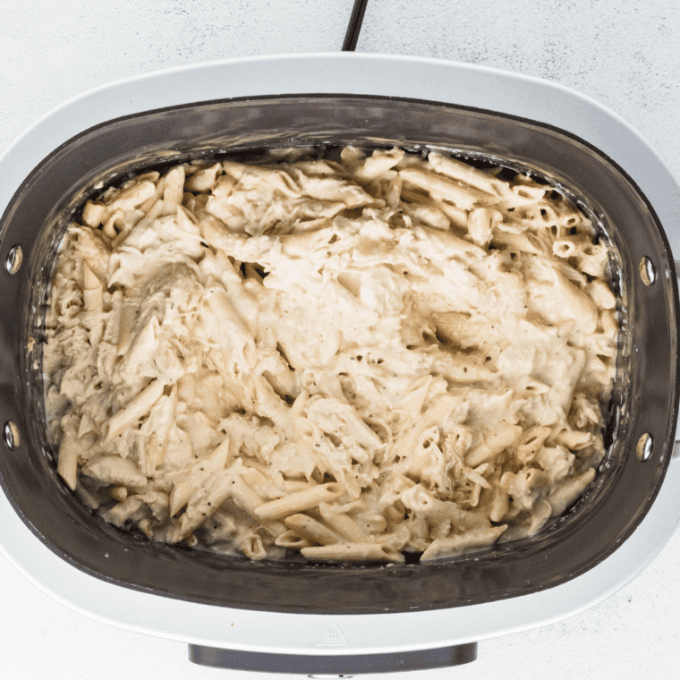 Cooking penne pasta and adding it to the slow cooker, stirring gently to coat with creamy chicken mixture.