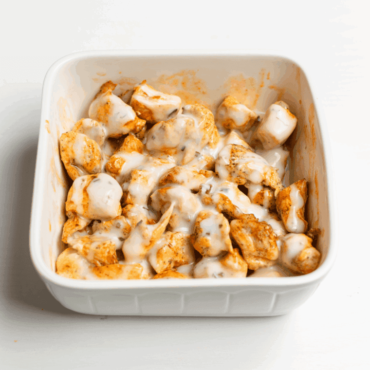 Placing buffalo-coated chicken in an oven-safe dish, drizzling with ranch or blue cheese dressing, and topping with shredded mozzarella and cheddar cheeses.