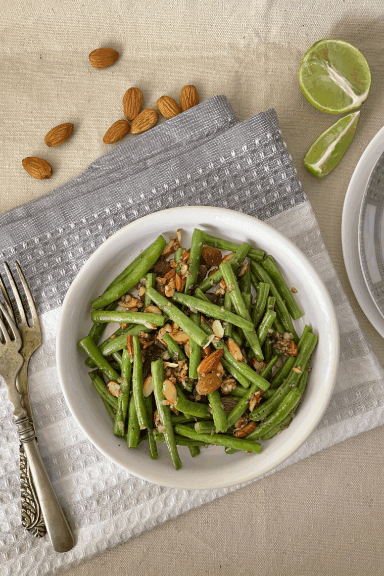 Crisp green beans and toasted almonds cooked in the air fryer, garnished with fresh parsley on a serving plate.